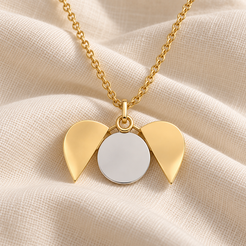 Gold angel wings pendant necklace with a blank silver circular center, displayed on a textured cream fabric background.