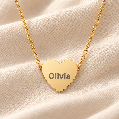 A gold heart-shaped pendant necklace engraved with the name 'Olivia' in dark lettering, resting on a textured beige fabric background.
